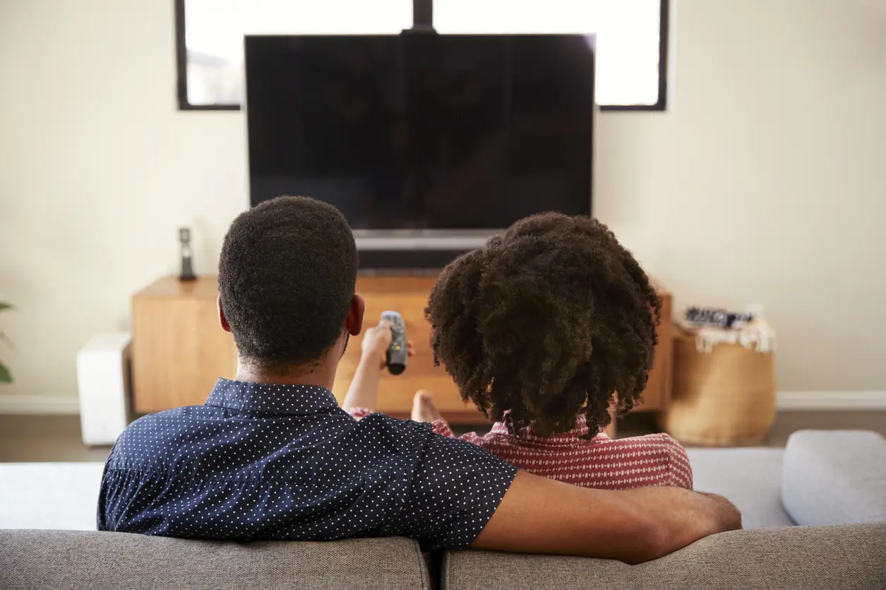 Rear View Of Couple Sitting On Sofa Watching TV Together